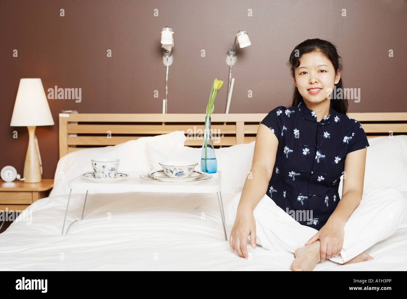 Portrait of a young woman sitting on the bed smiling Stock Photo - Alamy