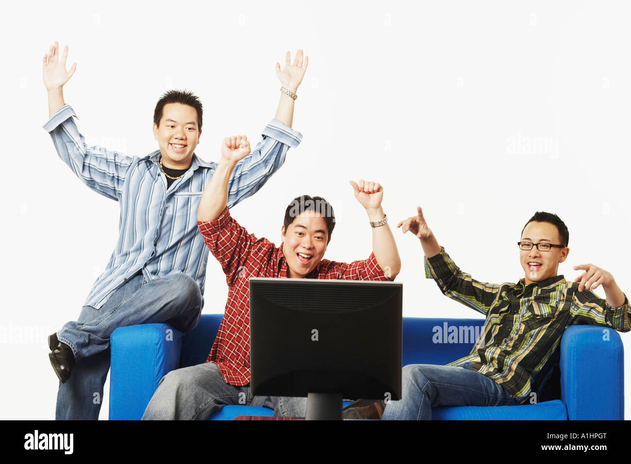Close-up of three young men cheering in front of a flat screen monitor Stock Photo