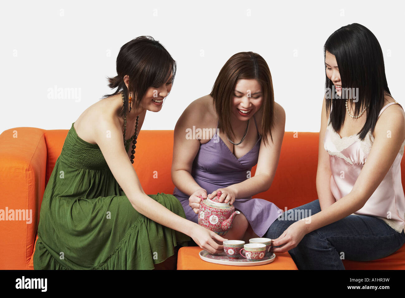 Three young women sitting on a couch with tea cups Stock Photo - Alamy