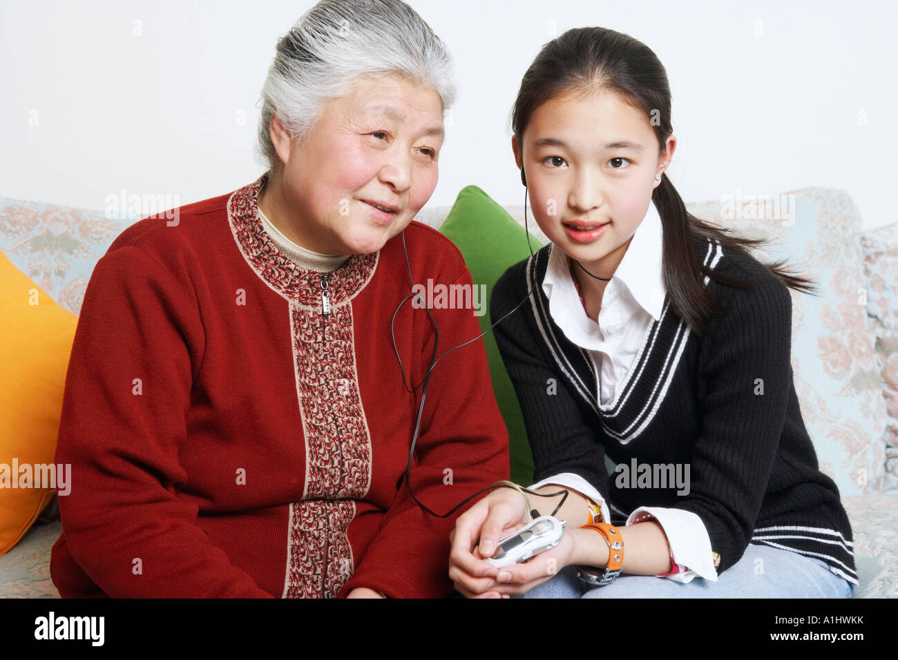 Portrait of a young woman sharing headphones with her grandmother Stock Photo