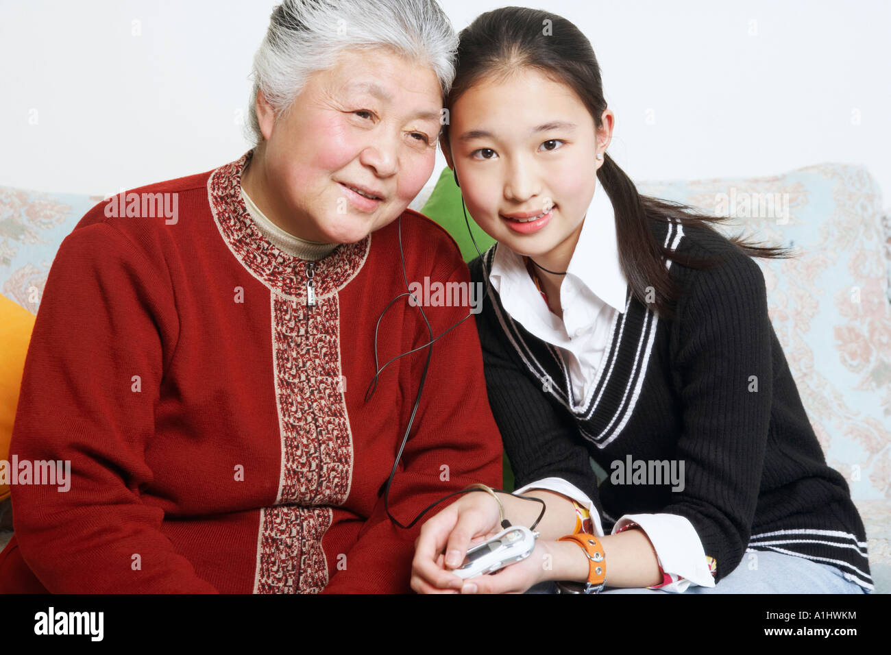 Portrait of a young woman sharing headphones with her grandmother Stock Photo