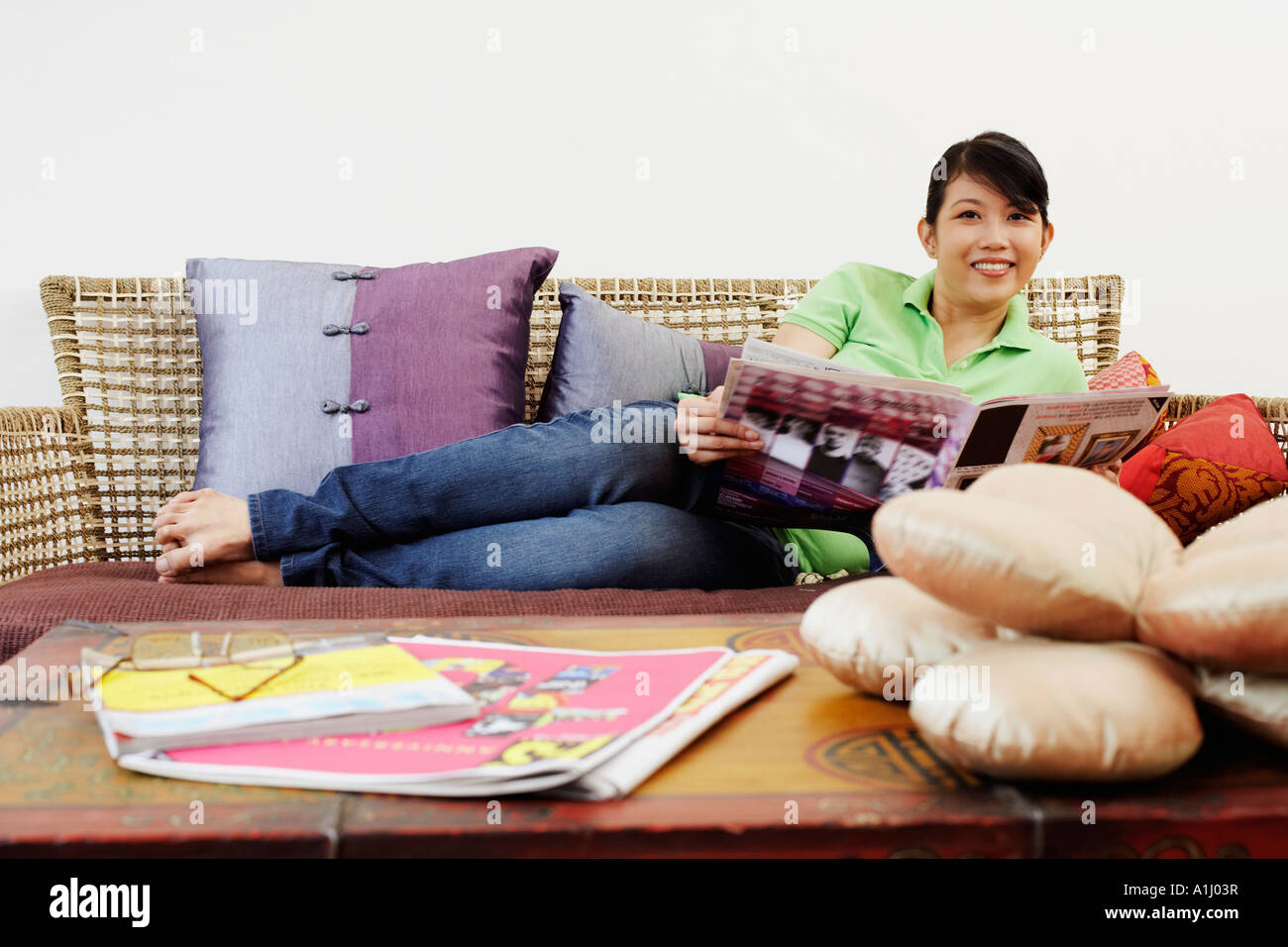 Portrait of a young woman reclining on a couch and holding a newspaper ...