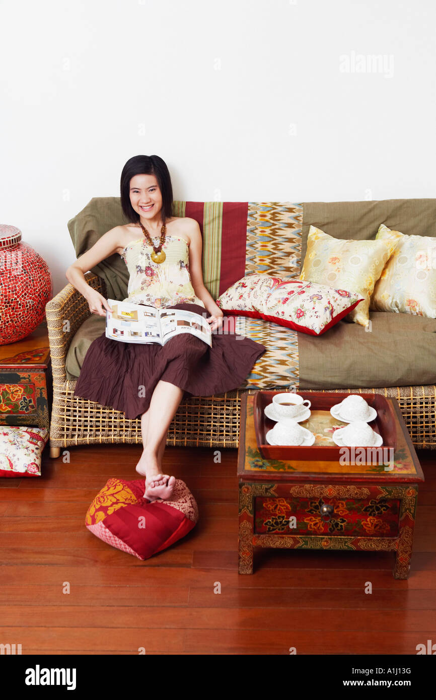 Portrait of a young woman sitting on a couch and holding a magazine ...