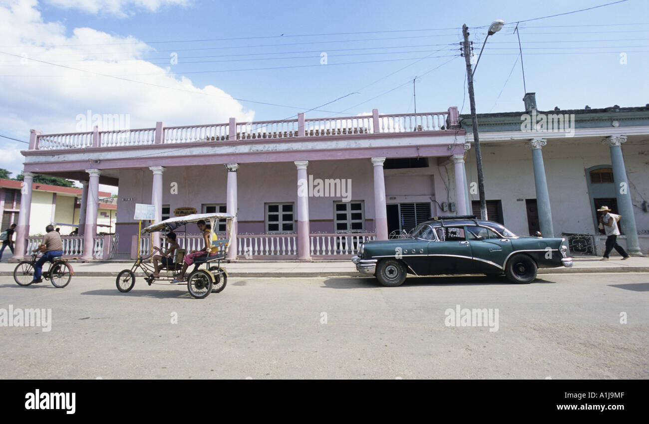 Streetscene in Jaguey Grande, Cuba. Local public transport in front of pink coloured , pillared, colonial houses. Stock Photo