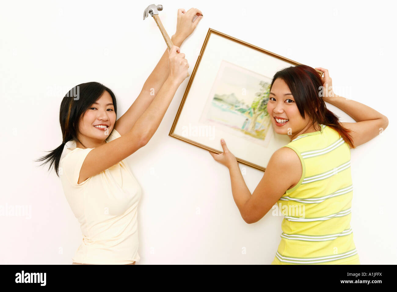 Portrait of two young women mounting paintings on a wall Stock Photo