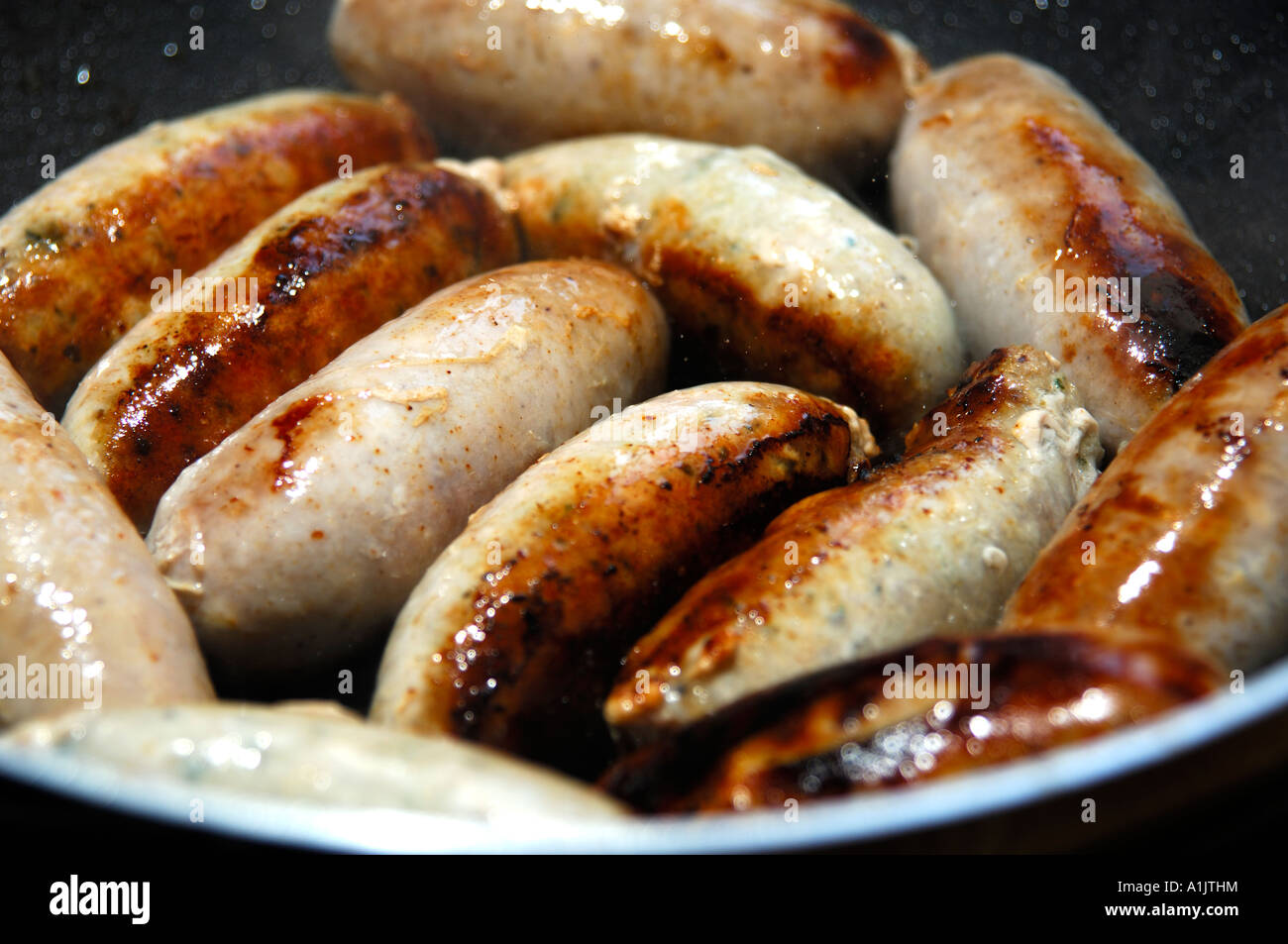 Thick pork sausages frying in a pan Stock Photo