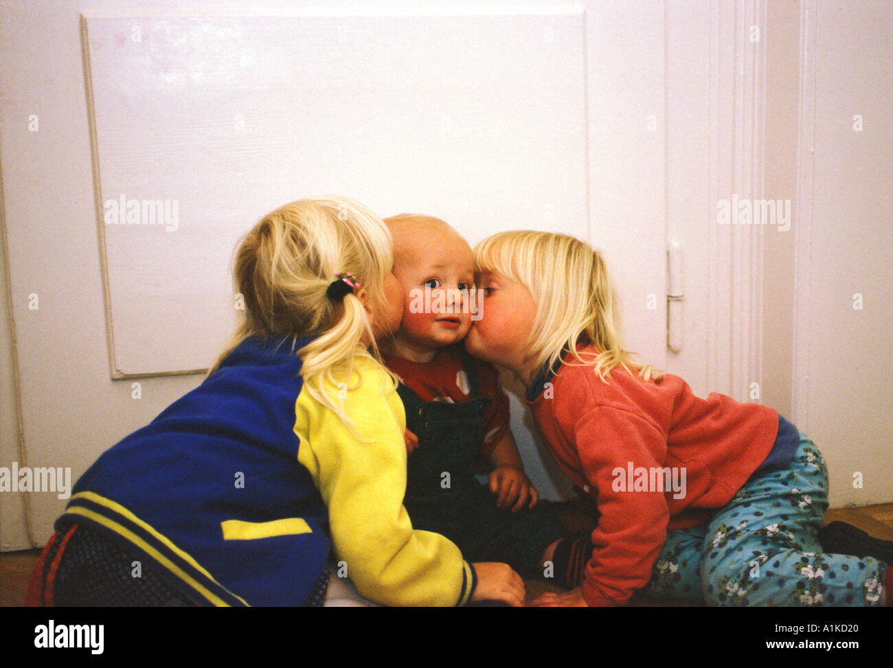 Two girls kissing one year old boy MR Stock Photo