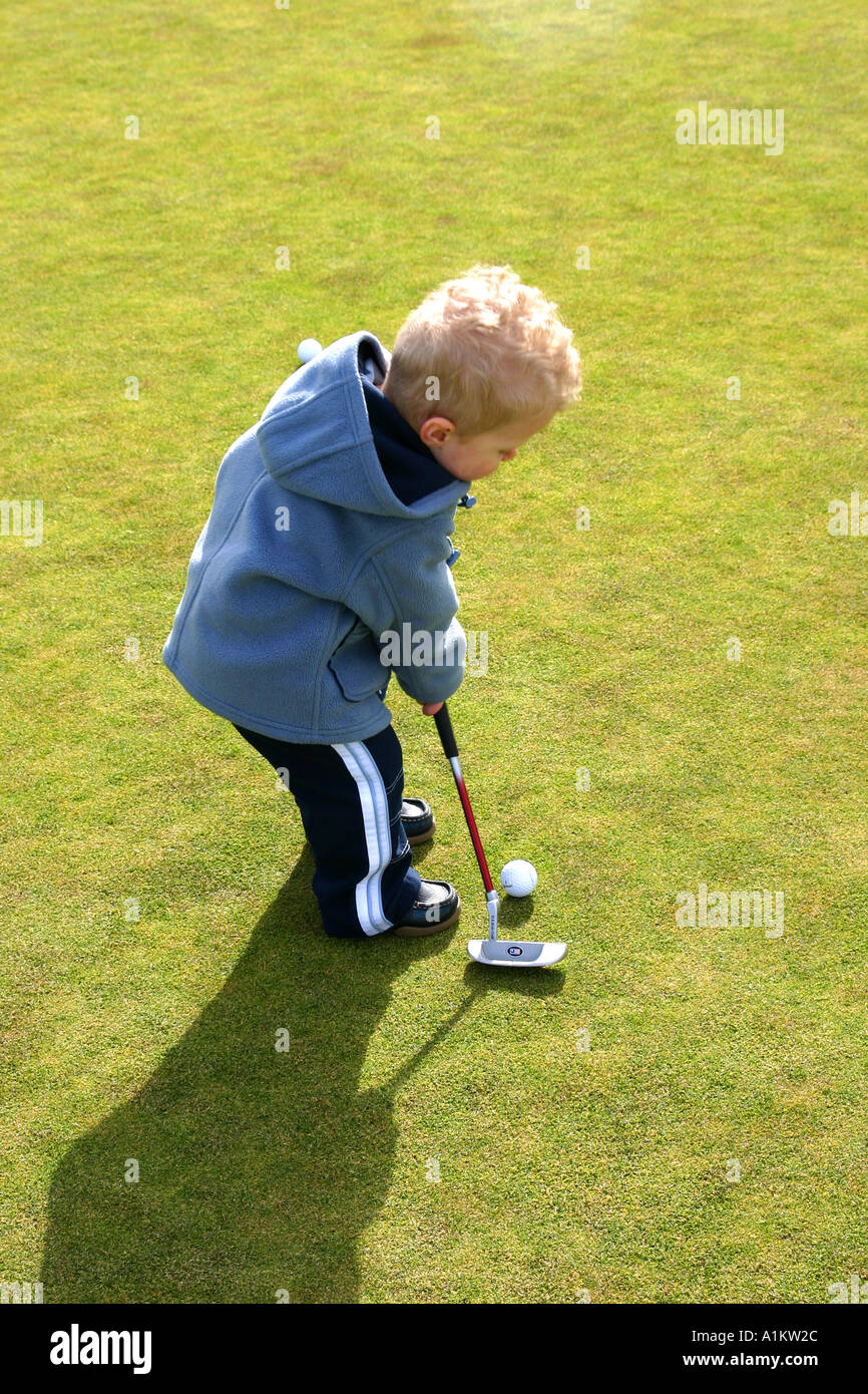 Toddler putting on a golf practice putting green Golf golfing putt putting put ball dimple coat winter spring baby toddler lea Stock Photo