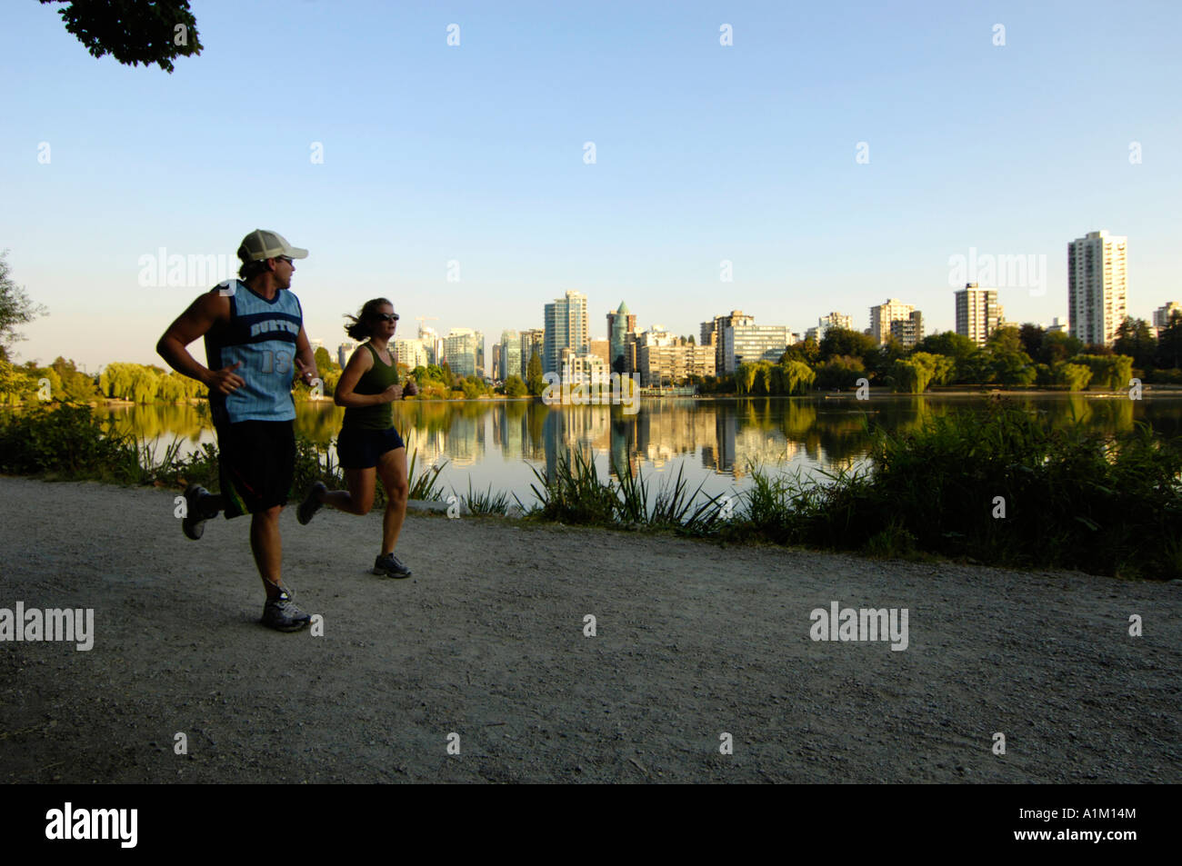 Runners at Lost Lagoon in Stanley Park with the Vancouver skyline behind, Vancouver BC, Canada Stock Photo