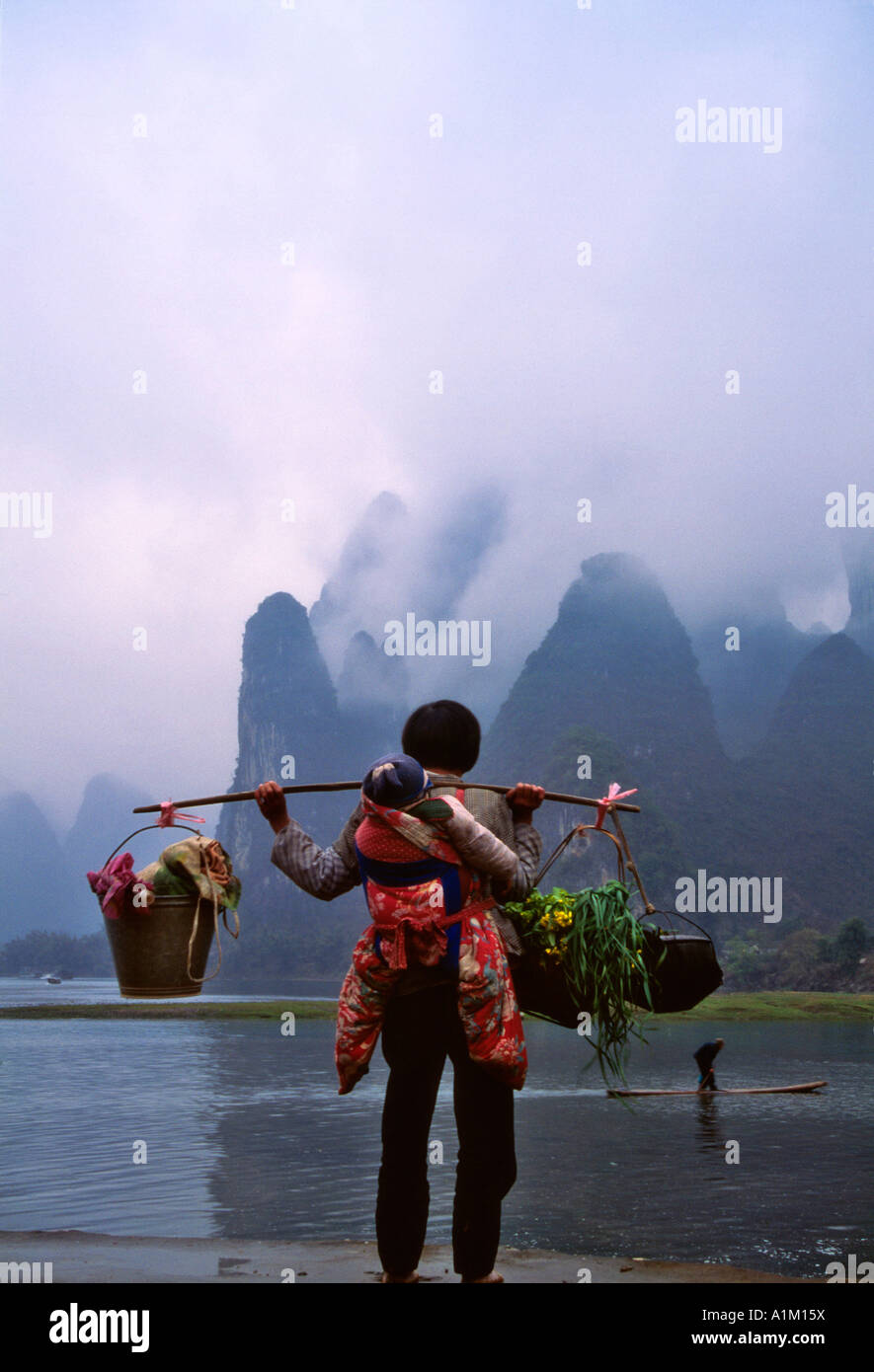 Woman carrying baby and shoulder pole by Li River Guangxi Province China Stock Photo