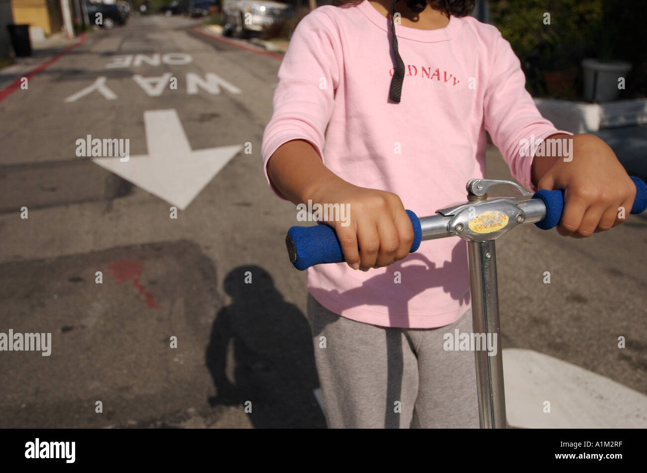 A girl riding a scooter down an alley with the one way sign and arrow
