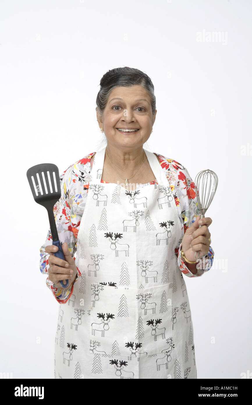 Indian old senior citizen with kitchen utensils wearing apron to cook