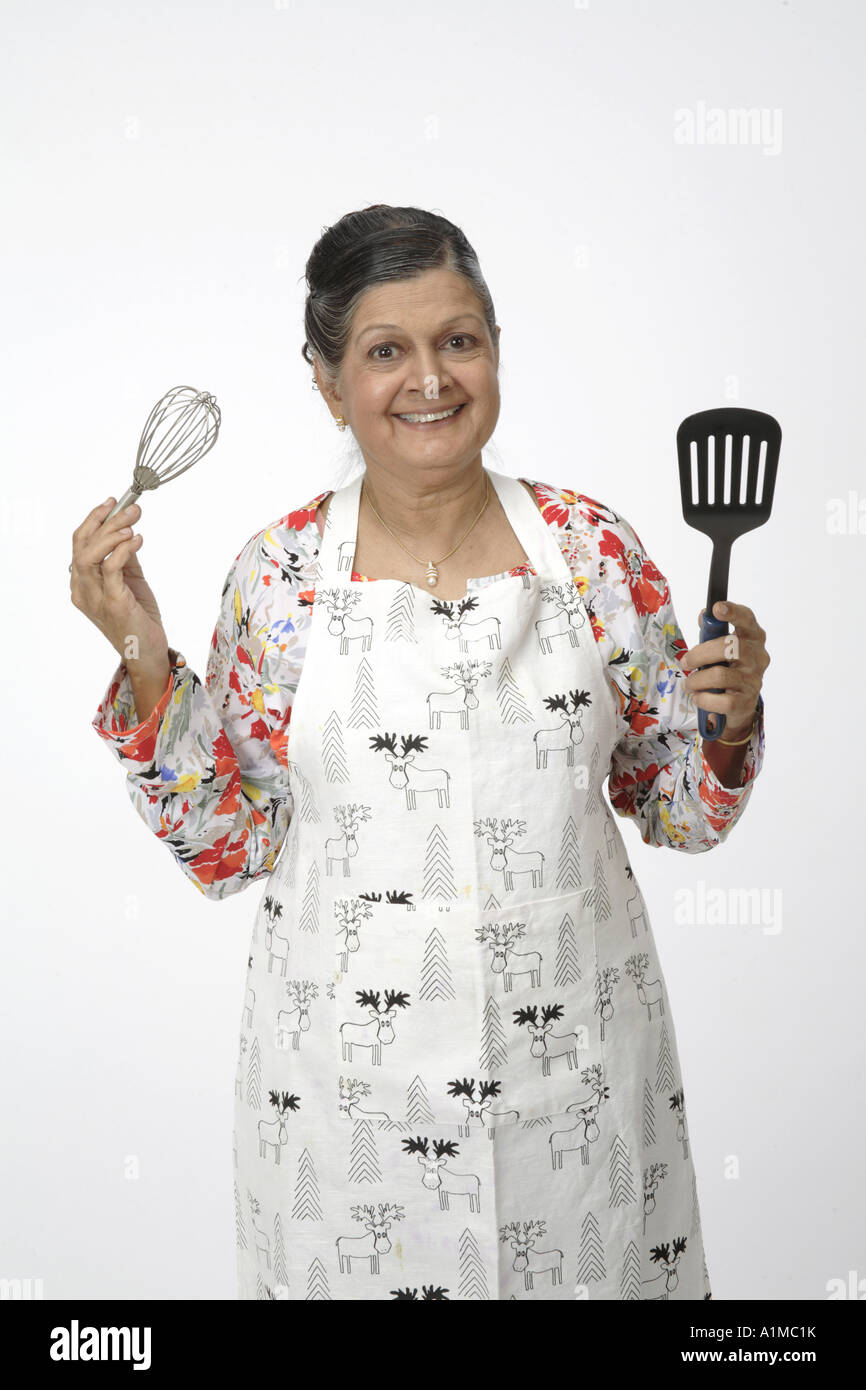 Indian senior citizen with kitchen utensils wearing apron to cook Stock