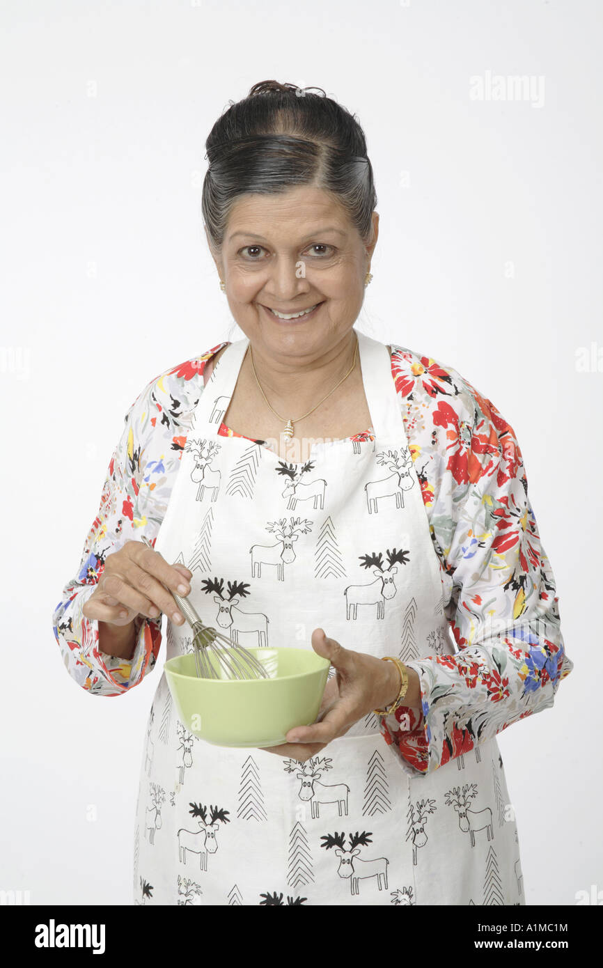 Indian senior citizen with kitchen utensils wearing apron to cook Stock