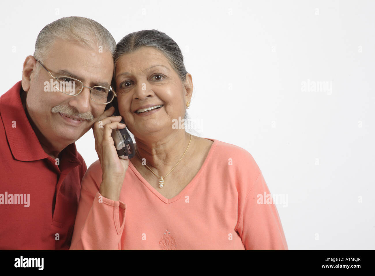 Indian senior citizen couple on phone on white background Stock Photo