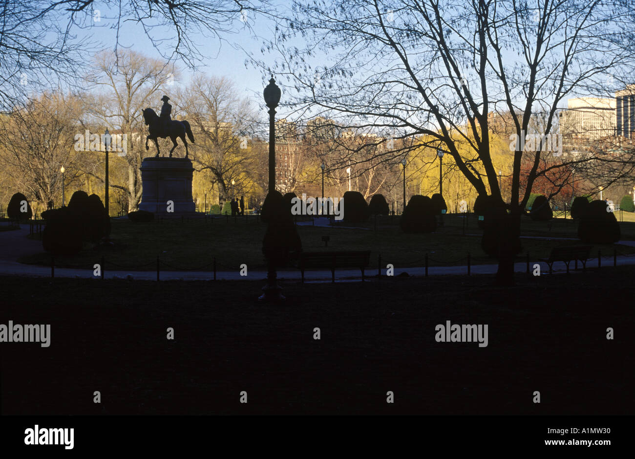 The shaded George Washington Statue in the Boston Public Garden is silhouetted against a well lit Beacon Hill Stock Photo