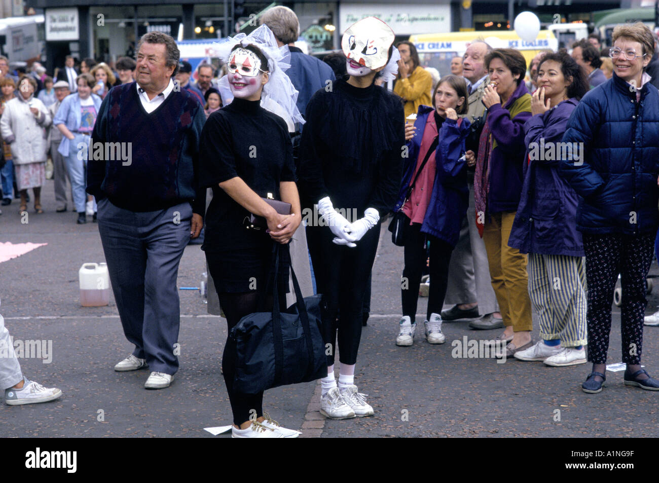 PERFORMERS IN B W COSTUMES EYE MASKS FACE PAINT IN A STREET PERFORMANCE PASSERBYS LOOK ON EDINBURGH FRINGE FESTIVAL Stock Photo