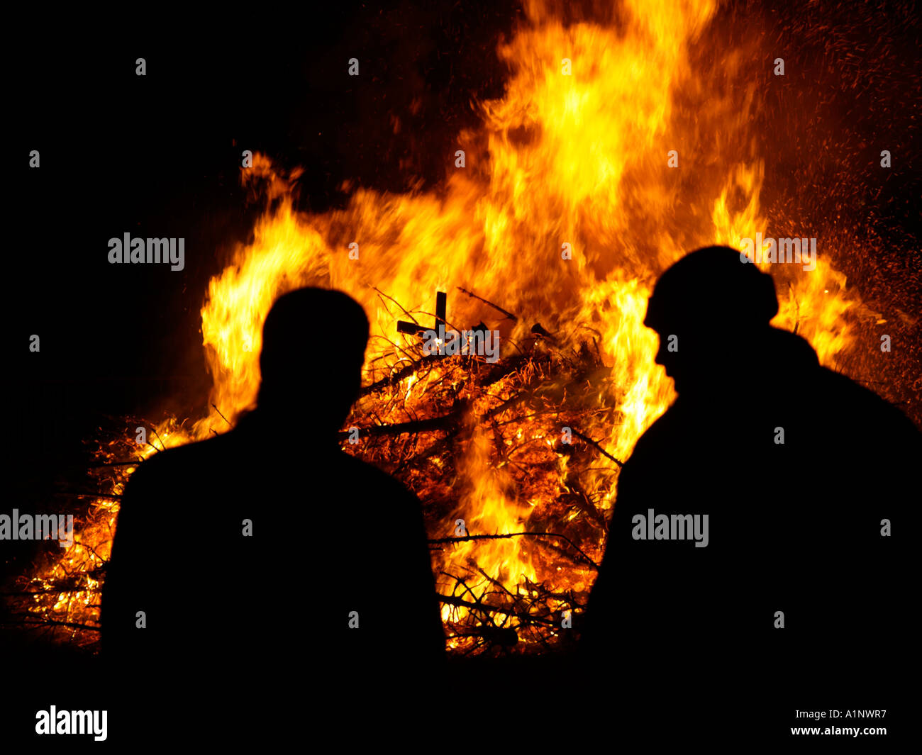 two men silhouetted in front of a huge fire bonfire from burning old christmas trees a custom in the Netherlands early january Stock Photo