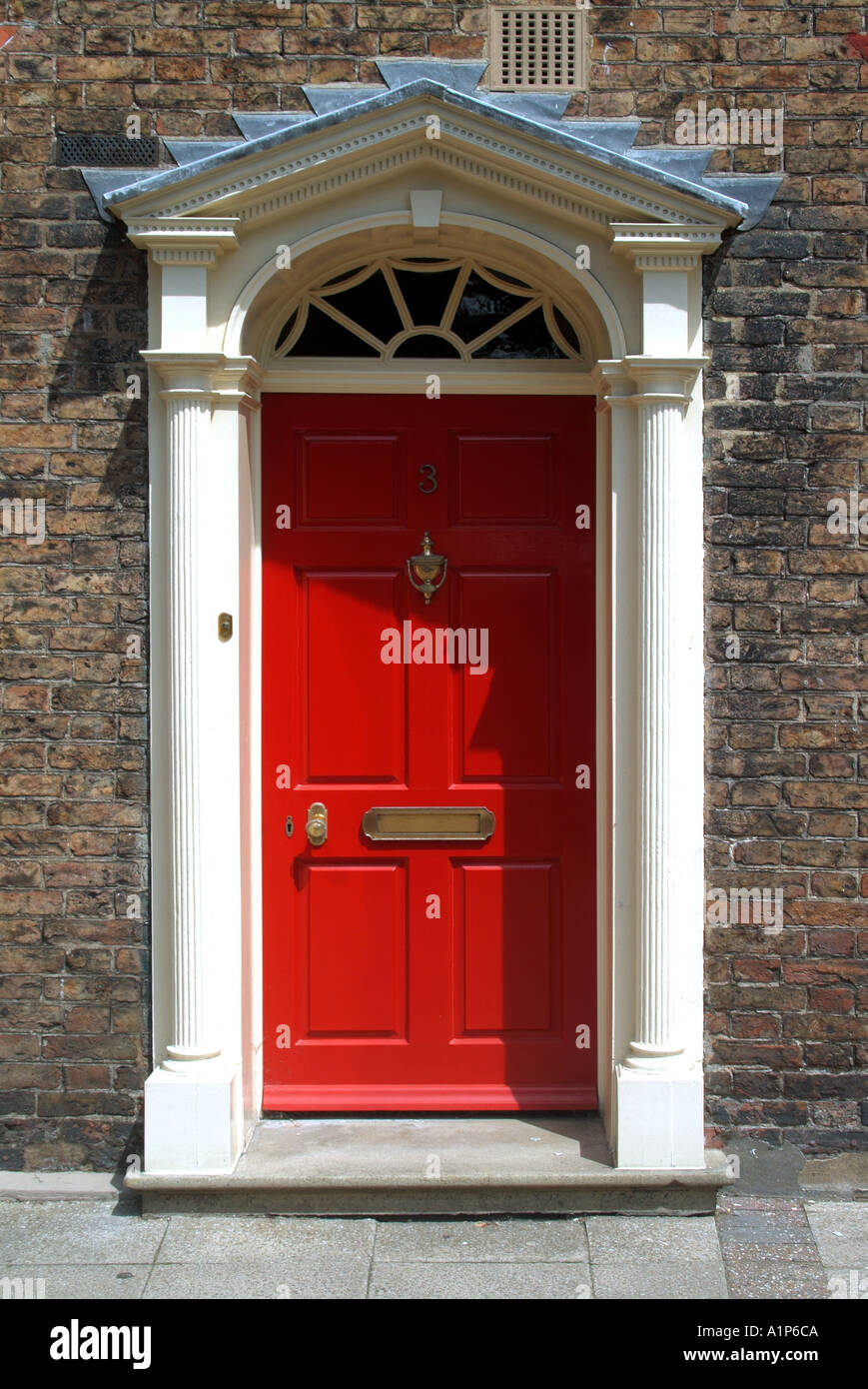 Red residential front door with white surround opening directly onto pavement Stock Photo