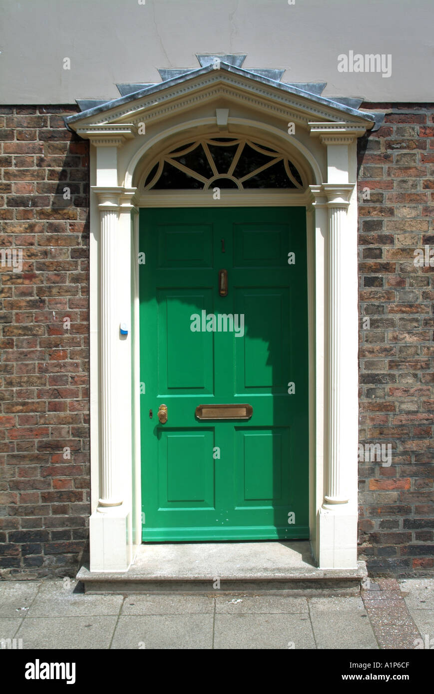 Green residential front door with white surround opening directly onto pavement Stock Photo