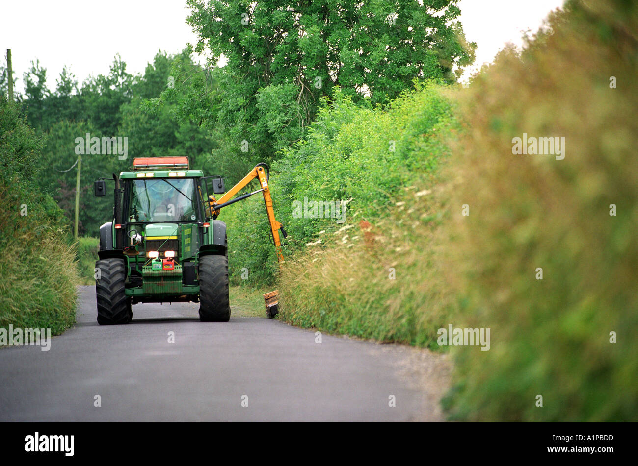 A tractor cutting back hedges on a country road in Britain UK Stock