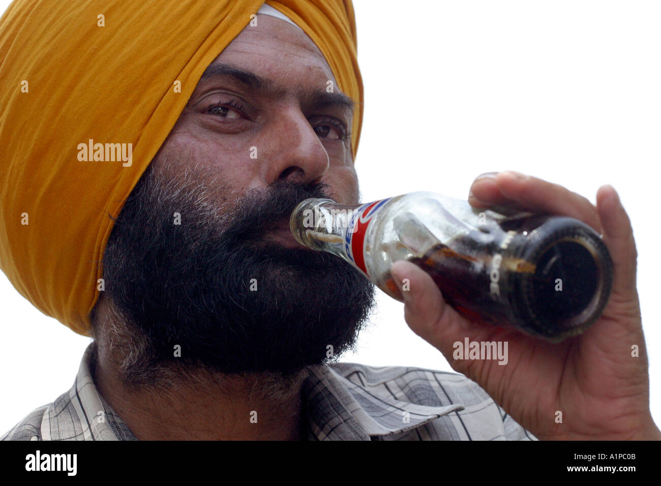 A Sikh man wearing a turban drinks from a persi cola bottle in New Delhi in India Stock Photo