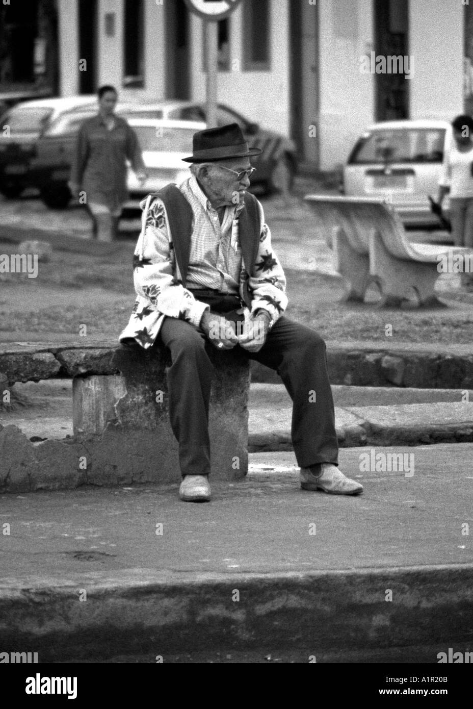 Senile man sitting outdoor on public bench waiting for time & people to go by Ciudad del Este Paraguay South Latin America Stock Photo
