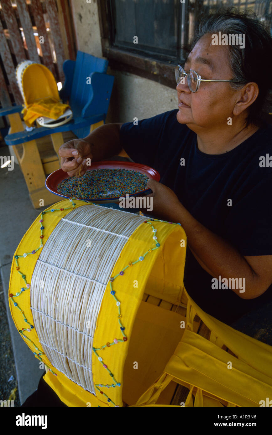 An Apache woman decorates a traditional baby cradle with beads on the