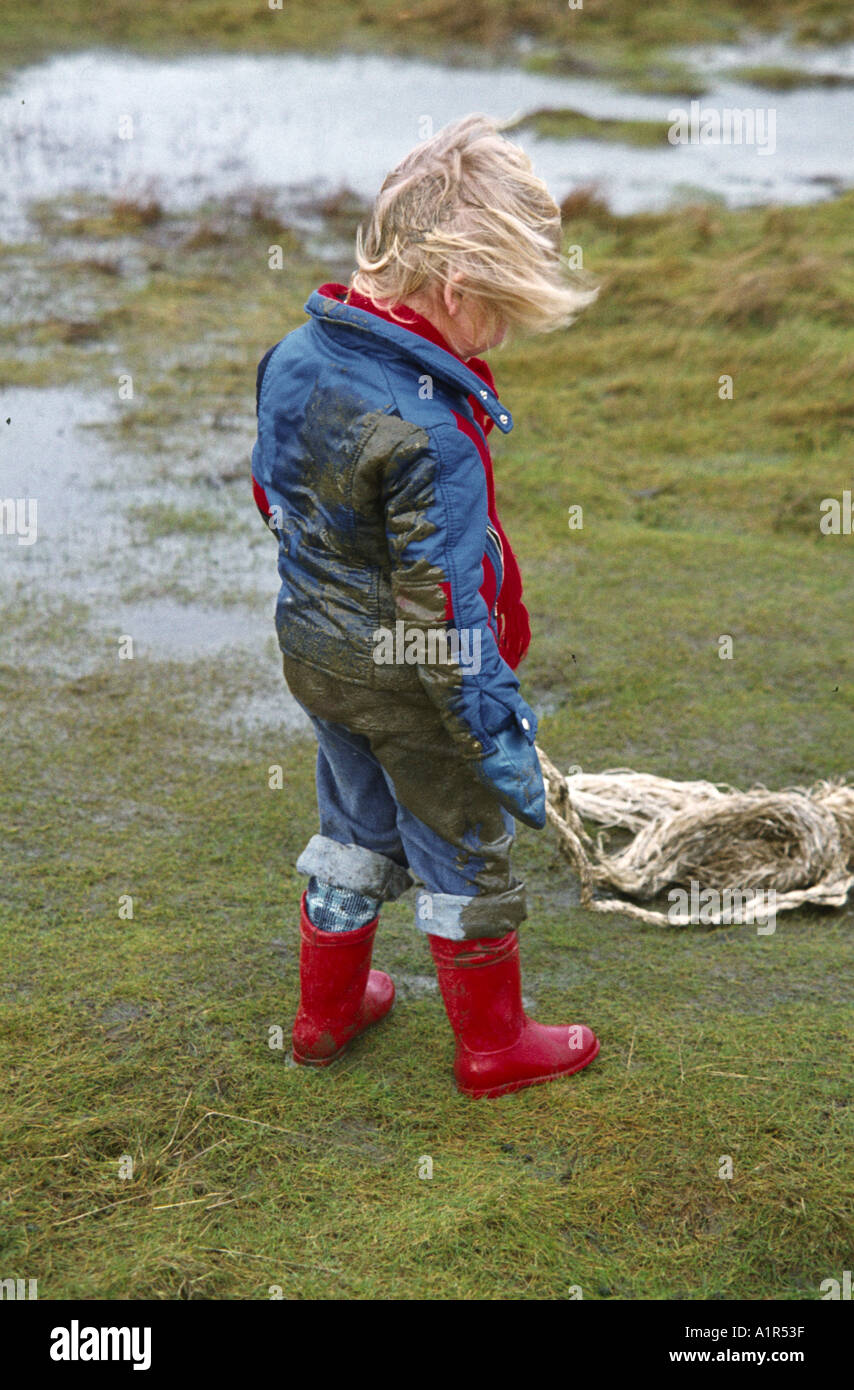 little boy with rubber boots and dirty raincoat playing on the beach