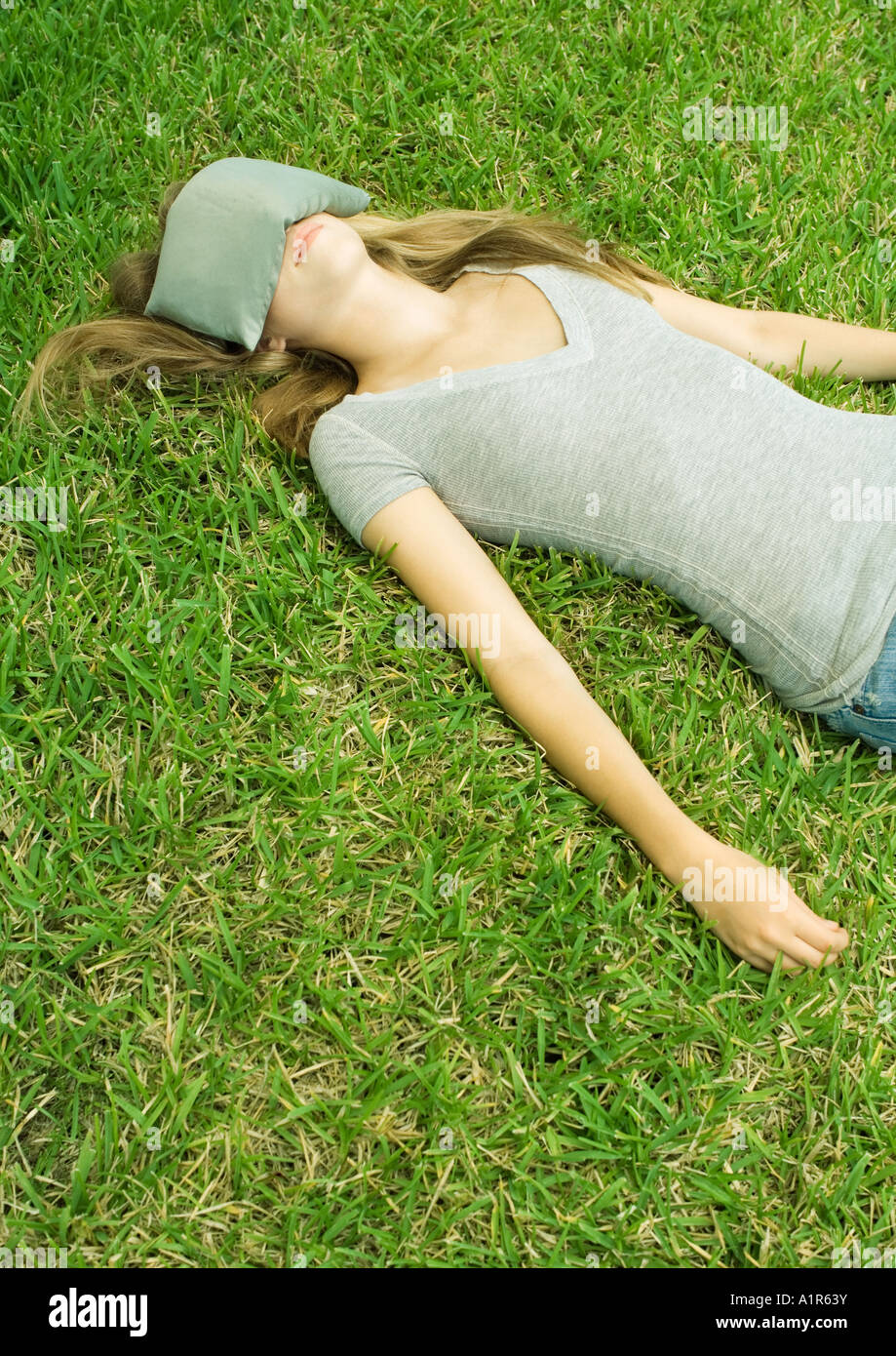 Young woman lying on grass with eye pillow covering eyes Stock Photo