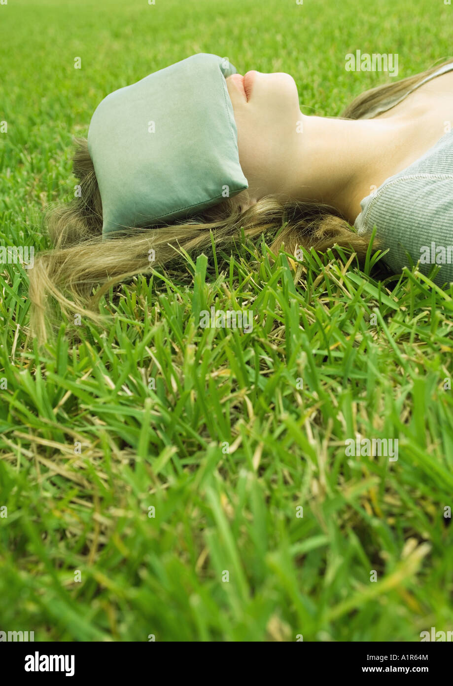Young woman lying on grass with eye pillow covering eyes Stock Photo