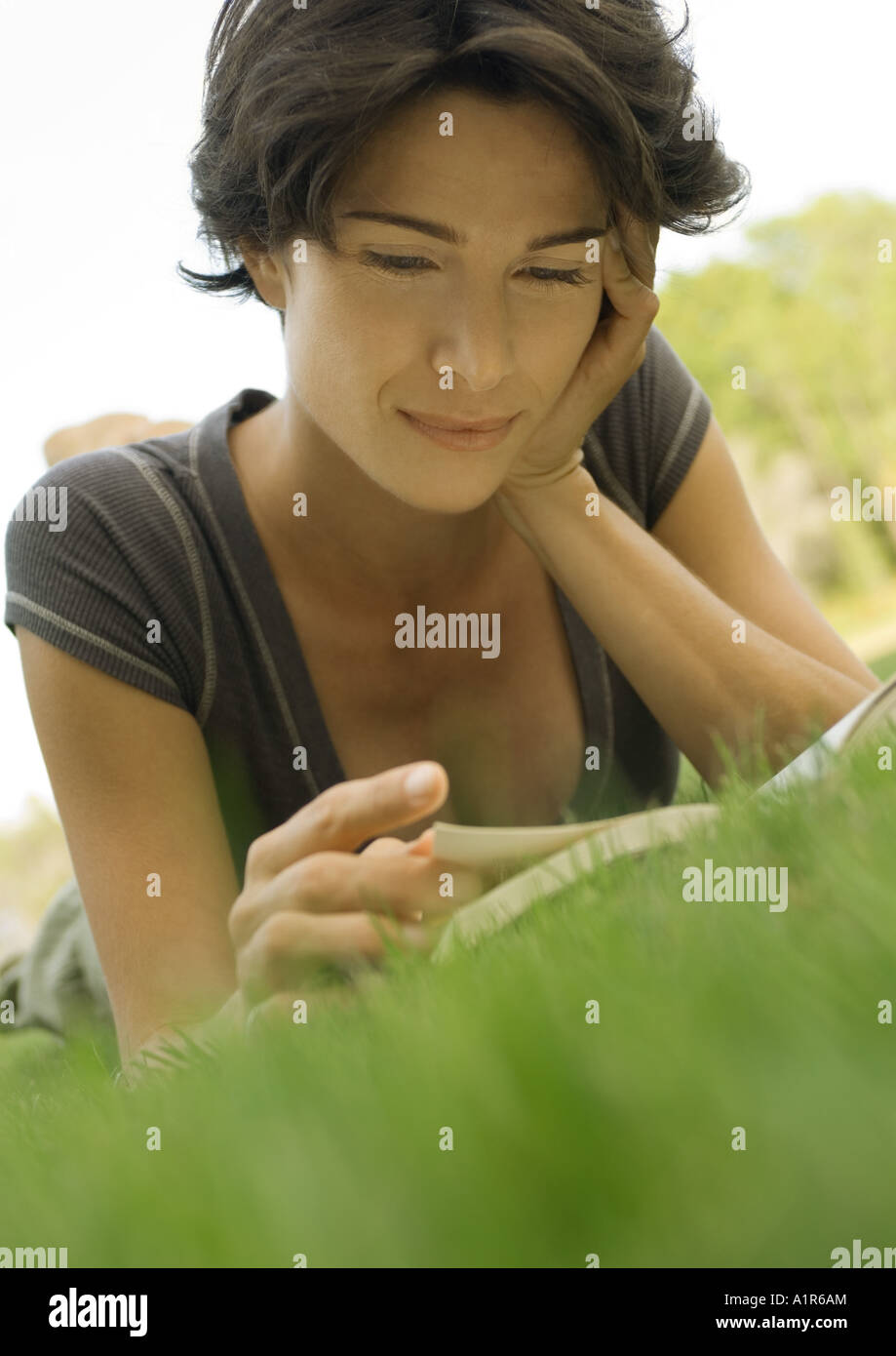 Woman lying in grass, reading book Stock Photo