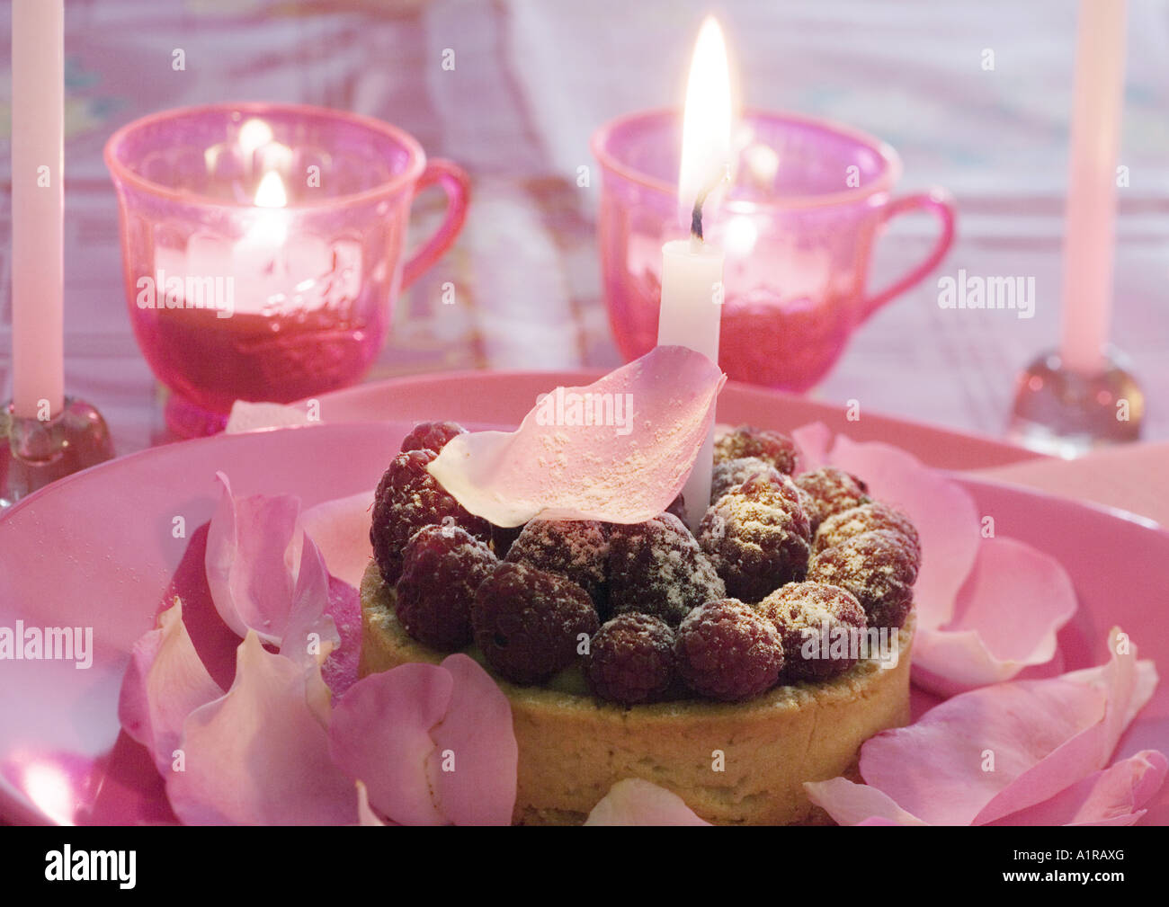 Raspberry tartlet on plate decorated with rose petals, surrounded with candles Stock Photo