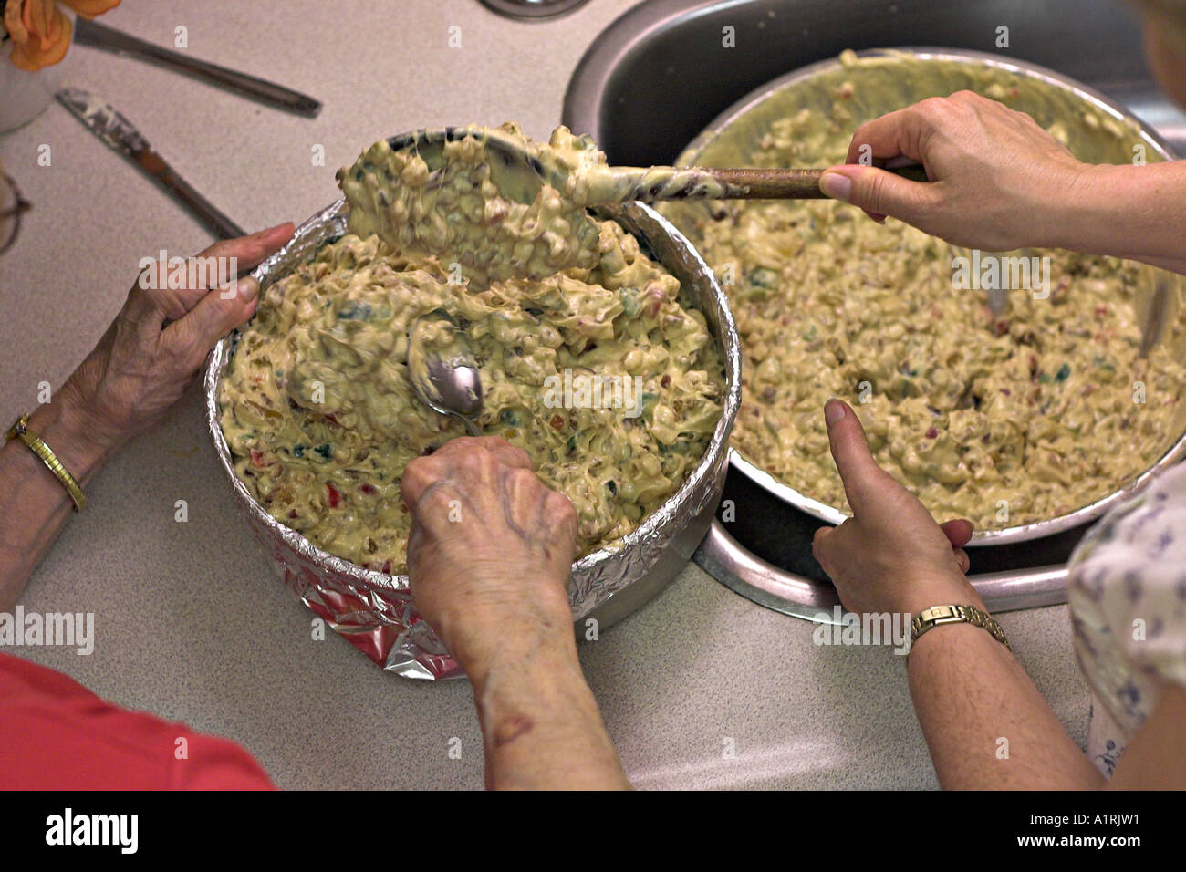 The four hands of a mother and daughter mix a wedding fruit cake and scoop it into a cake pan Stock Photo