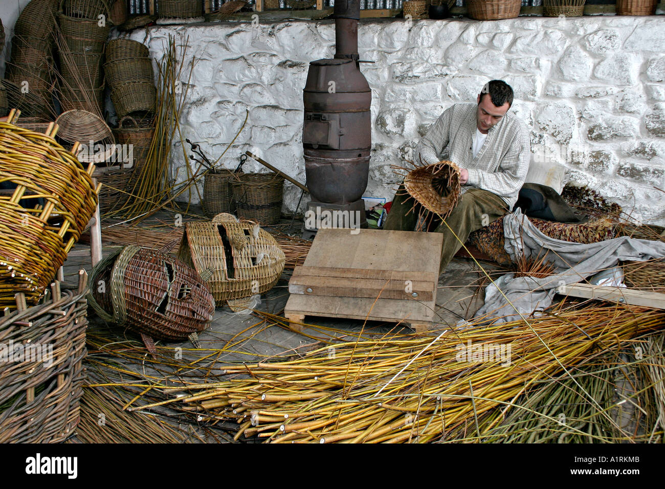 The Basket Weaver: A traditional basket weaver surounded by willow strips completed baskets and masks Stock Photo