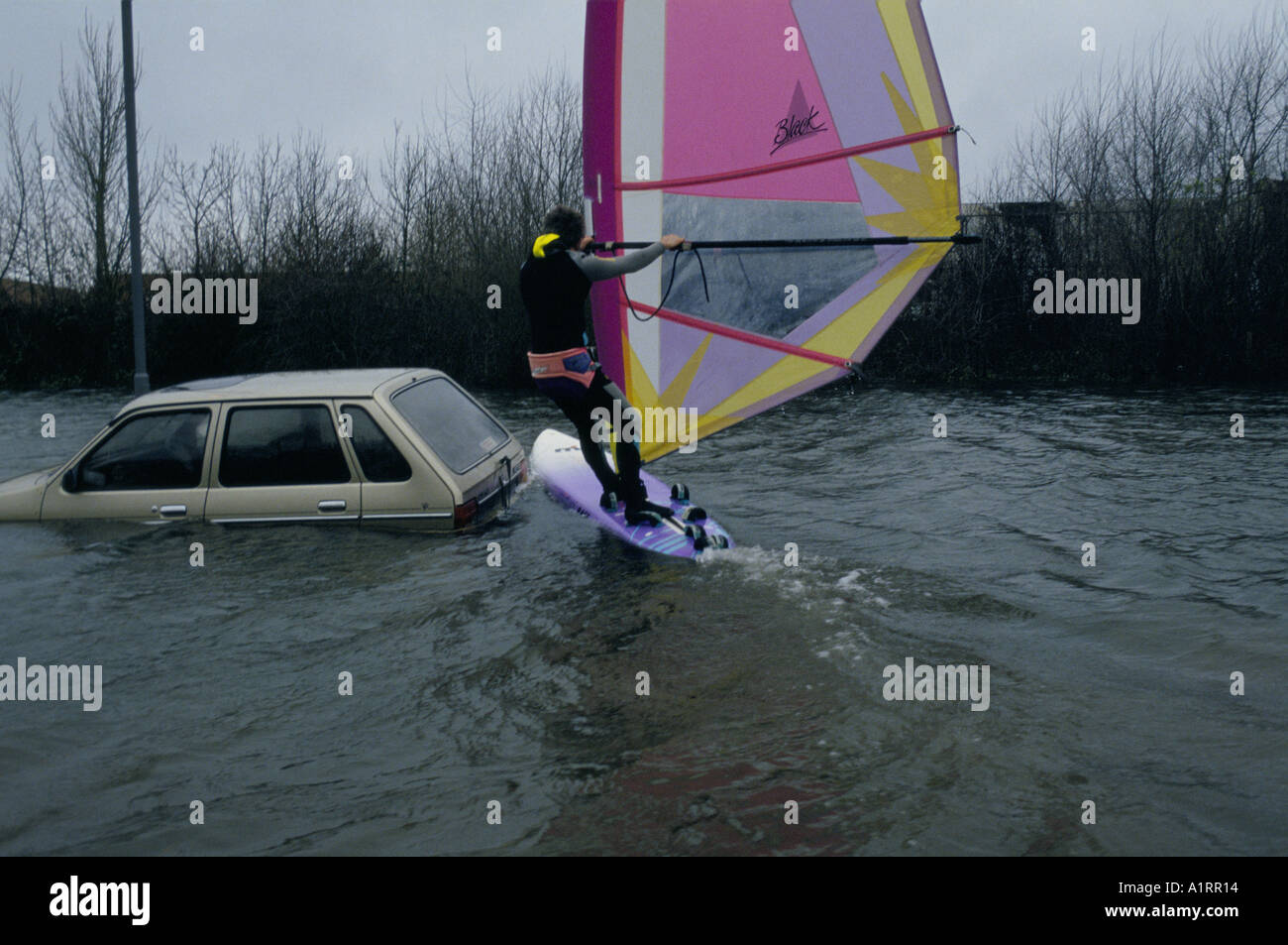 MAN WINDSURFING DURING FLOODING ON THE A27 ROAD BY AN ABANDONED BEIGE