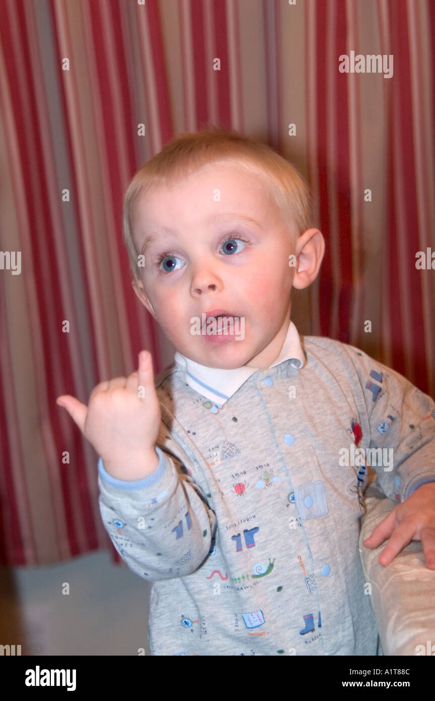 An infant boy in gray pajamas conversing with someone and making a hand signal for Hang Loose Stock Photo