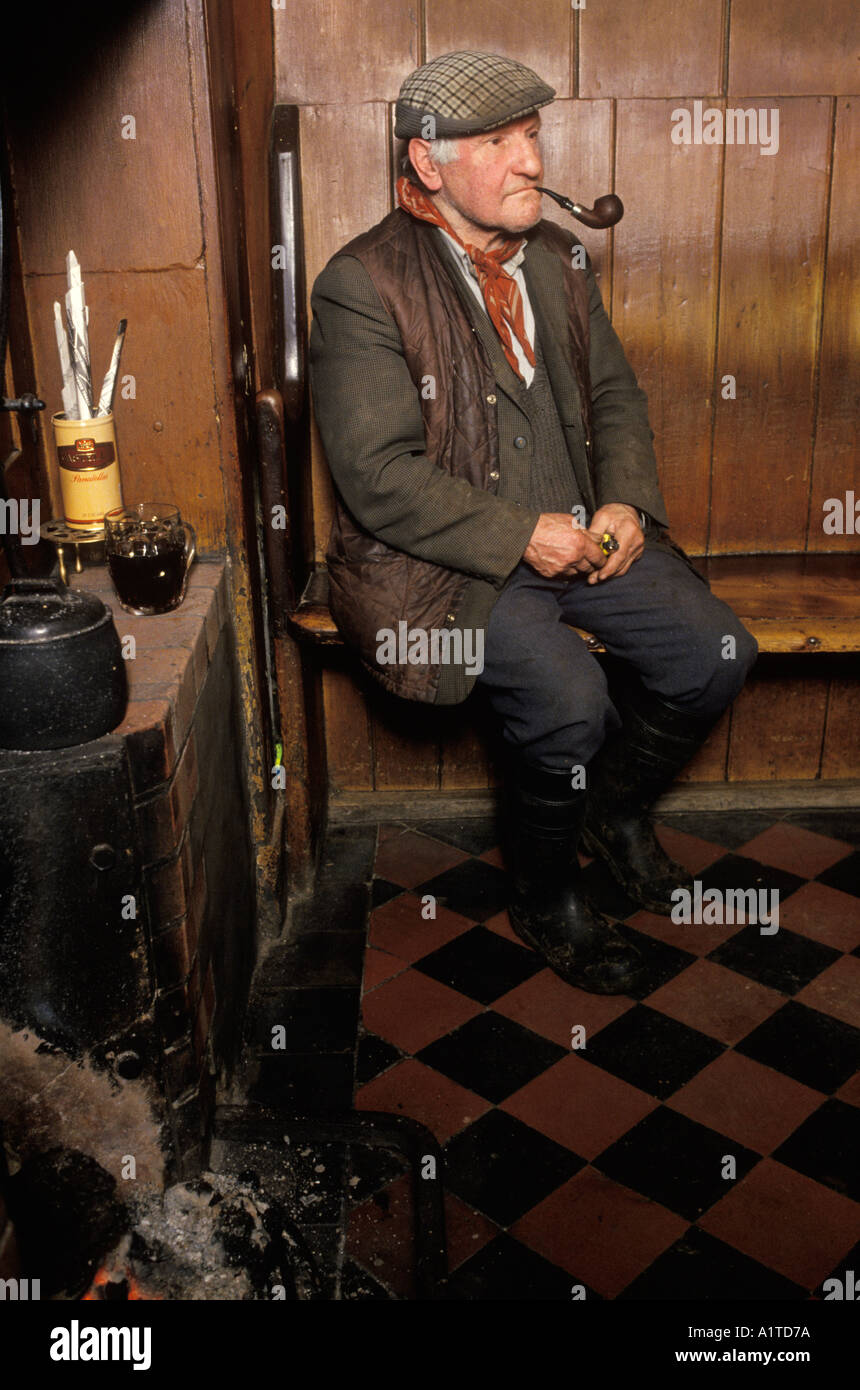 1980s pub interior UK. Kings Head public house Laxfield Suffolk. Smoking a pipe sitting on a high backed wooden settle bench.1985.   HOMER SYKES Stock Photo