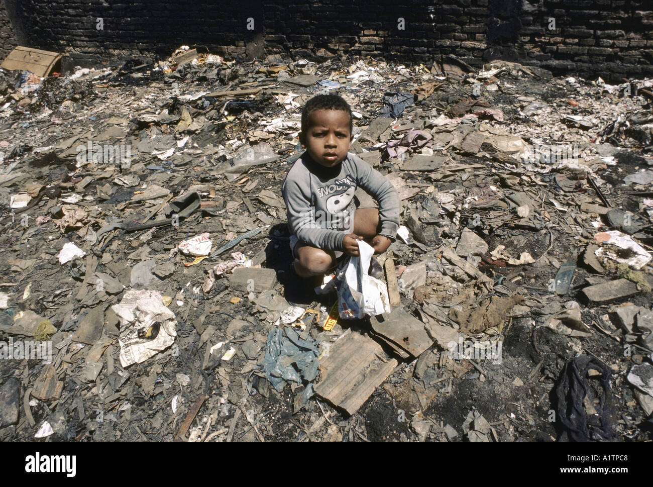 BRAZIL SAO PAULO SHANTY TOWN CHILD WEARING A SNOOPY SWEATER PLAYING IN RUBBISH Stock Photo