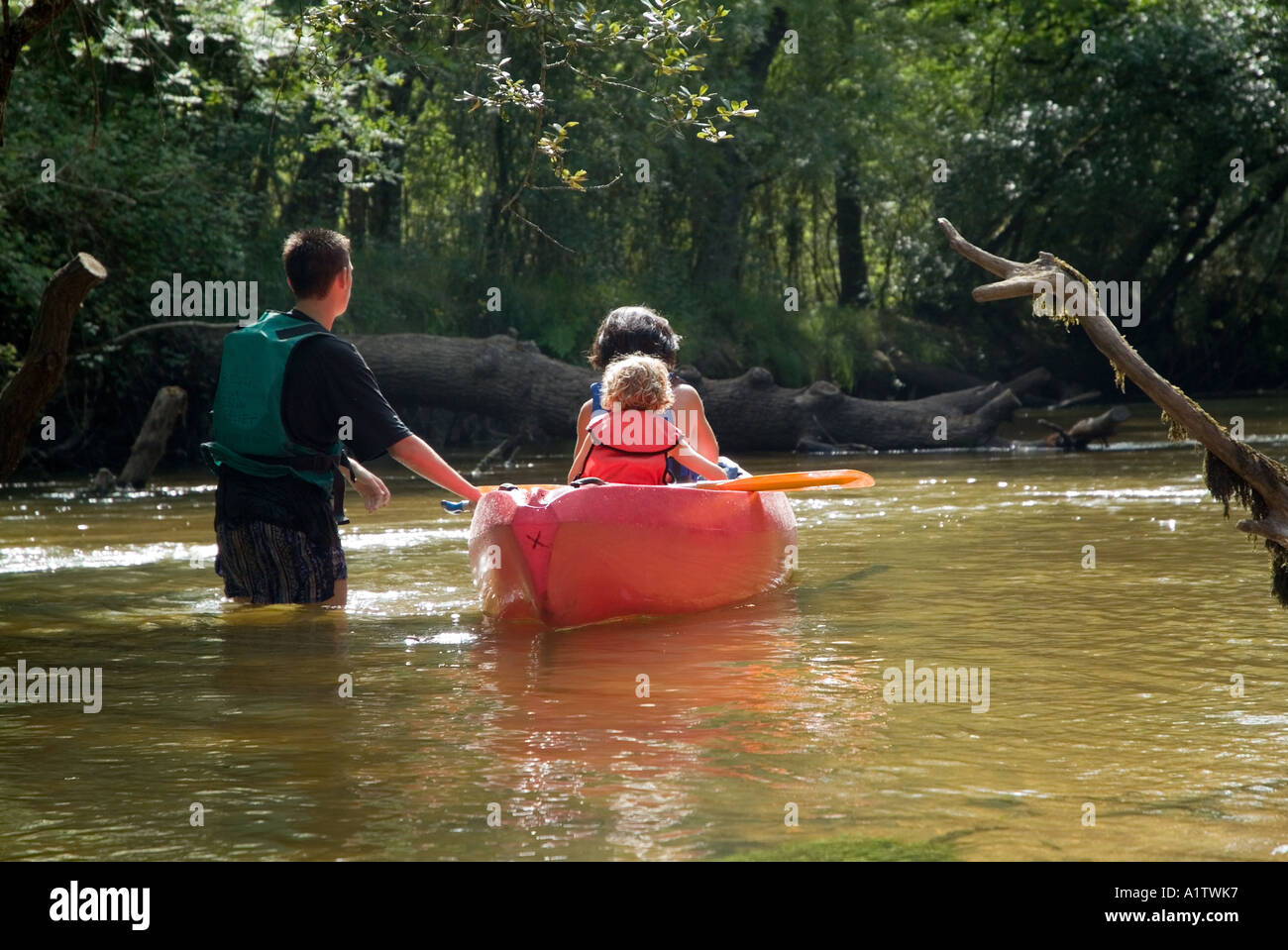 Rear view of two girls sitting in a canoe and a boy pushing it France ...