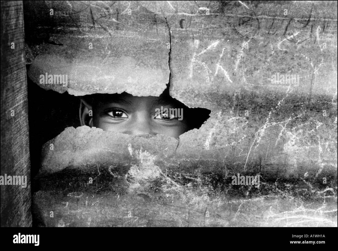 Child displaced by war peeks through gap in corrugated iron sheeting of refuge where he lives Liberia Monrovia Stock Photo