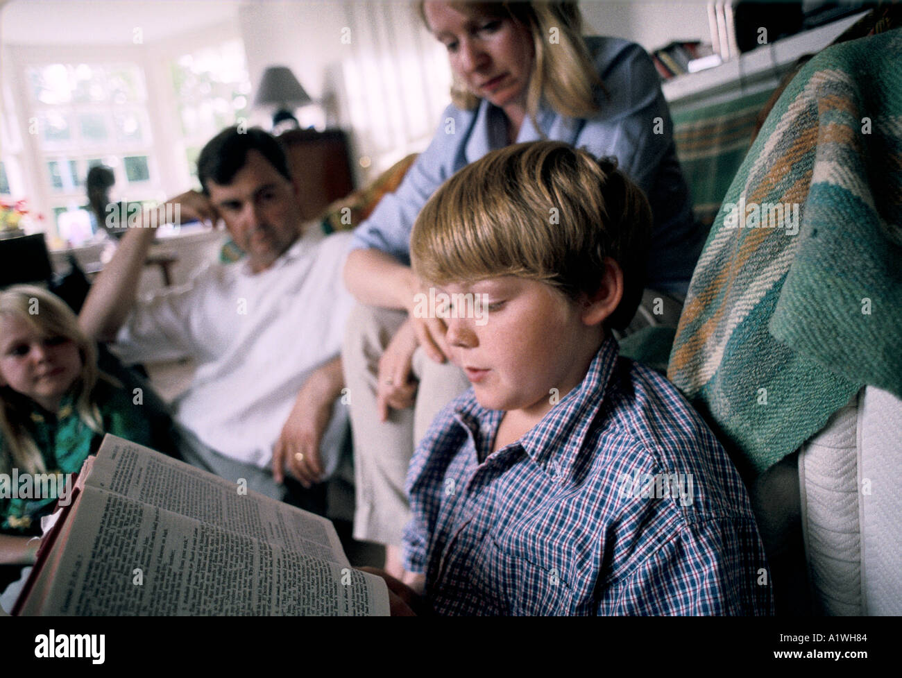 BOY READING BIBLE WITH FAMILY AT HOME Stock Photo