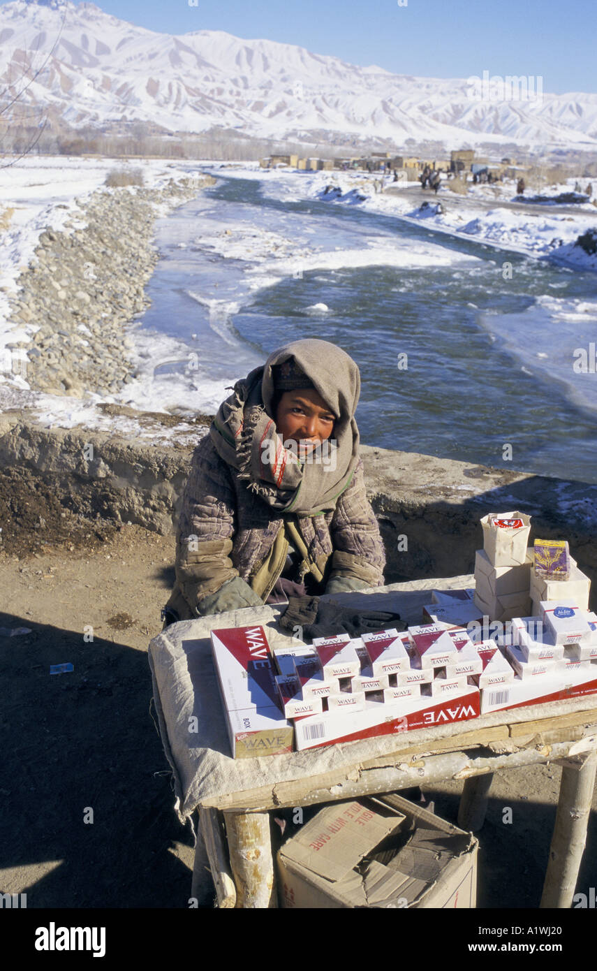 cigarettes in afghanistan BAMIYAN AFGHANISTAN 1998. Boy selling cigarettes in the market next to  frozen river, in front of snow covered mountains Stock Photo
