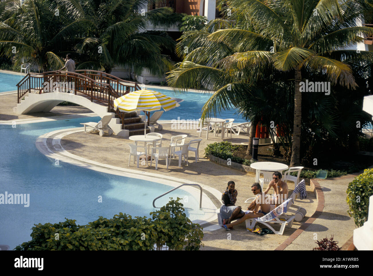 CUBA TWO MEN TALKING WITH LOCAL WOMAN BESIDE OUTDOOR SWIMMING POOL OF