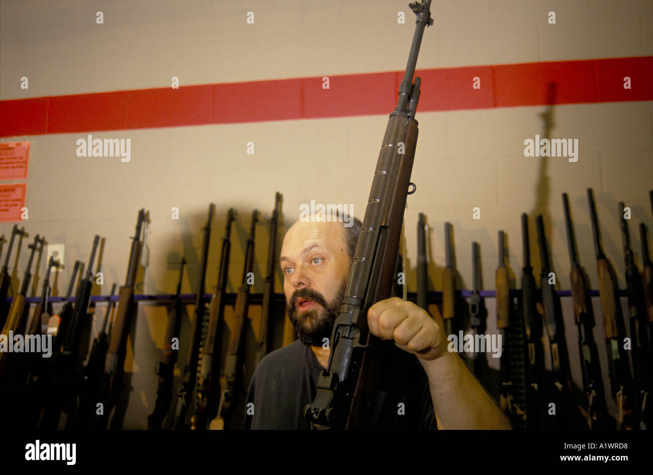 BEARDED MAN HOLDING A RIFLE IN A GUN SHOP WHERE HE WORKS Stock Photo