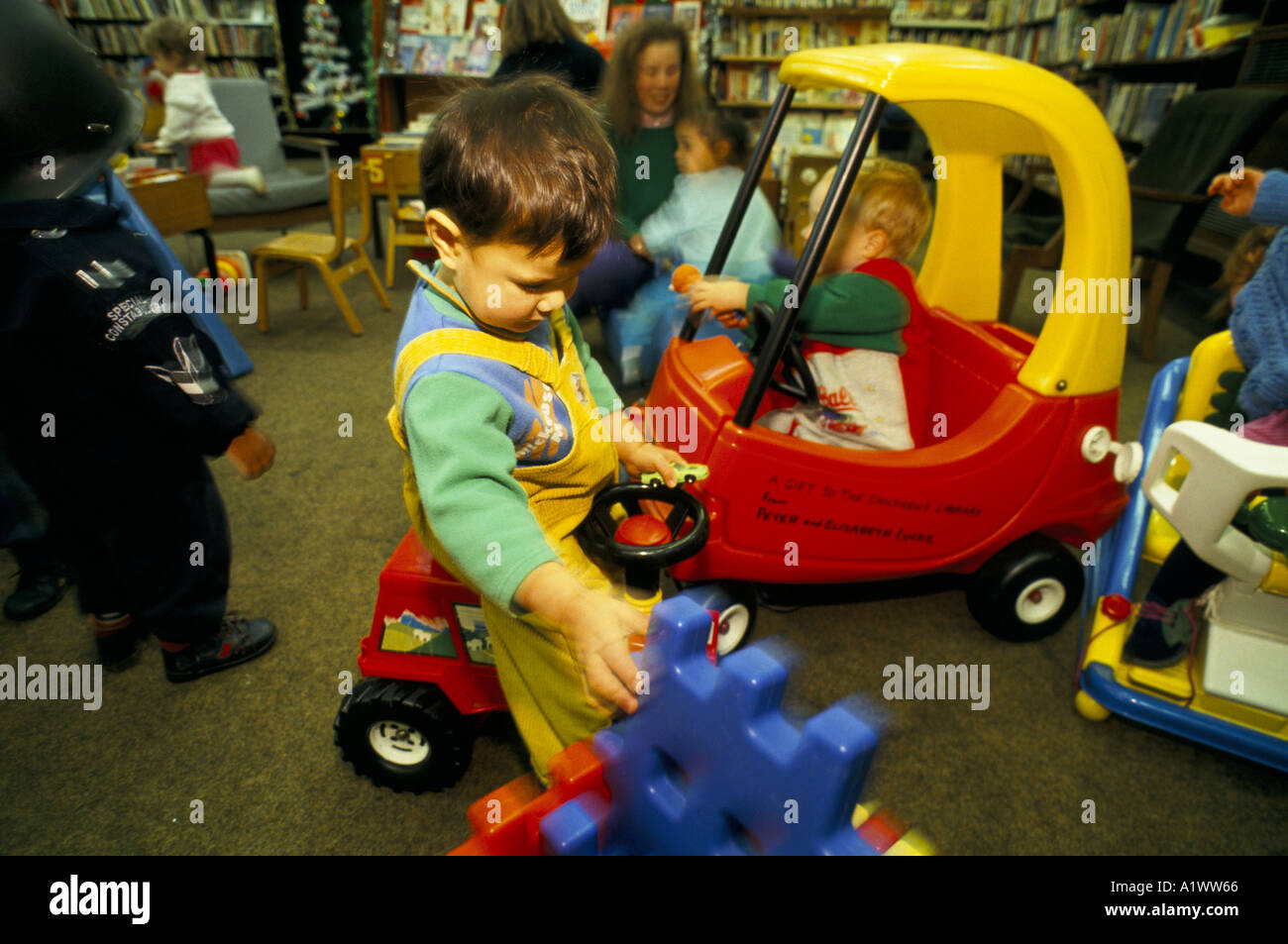 CHILDREN DRIVING PLASTIC CARS TOY  LIBRARY MUSWELL HILL LONDON Stock Photo
