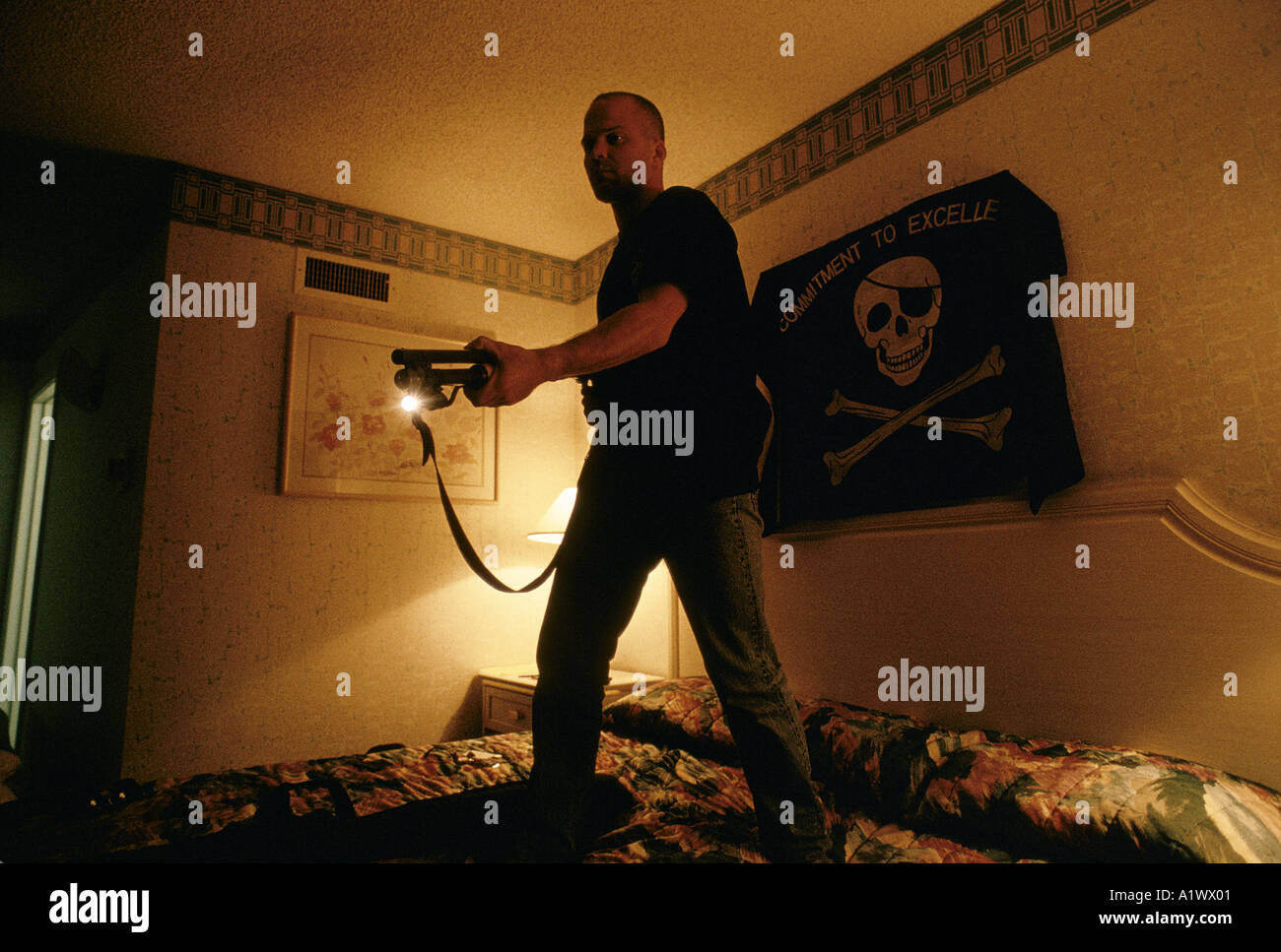 SOLDIERS OF FORTUNE CONVENTIONEER IN HIS HOTEL ROOM PLAYING WITH THE GUNS HE OWNS THE FLAG ABOVE THE BED IS OF HIS DESIGN THE SLOGAN READS commitment to excellence the 15th anniversary of soldier of fortune magazine annual convention sands hotel las vegas 1994 Stock Photo