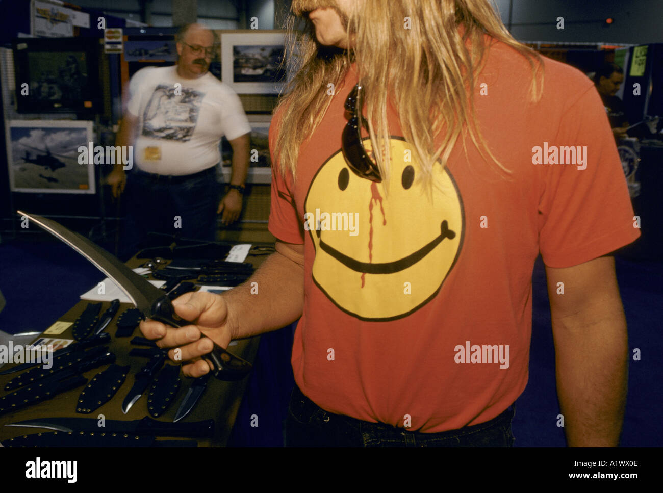 SOLDIERS OF FORTUNE CONVENTIONEER AT ONE OF THE MANY CUSTOM KNIFE STALLS WEARING SMILEY T SHIRT WITH BULLET IN FOREHEAD THE 15TH ANNIVERSARY soldier of fortune magazine annual convention sands hotel las vegas summer 1994 Stock Photo