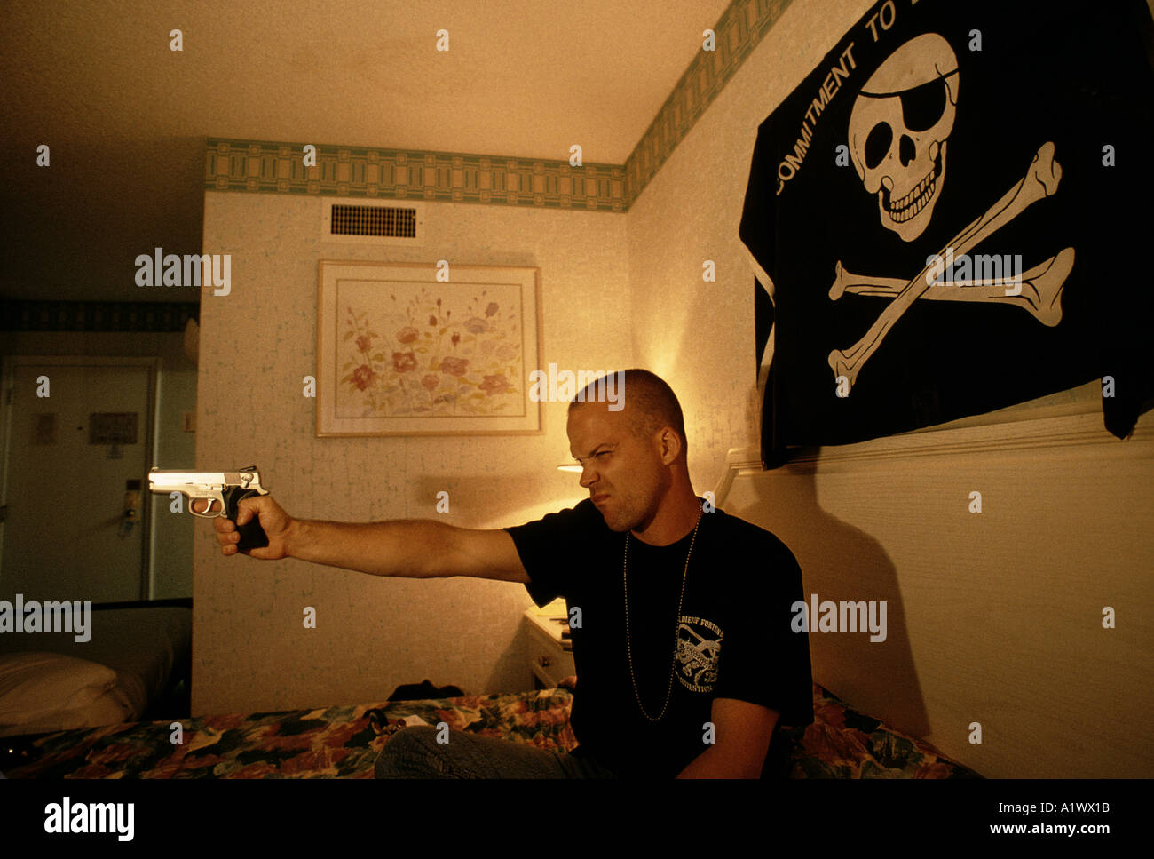 SOLDIERS OF FORTUNE YOUNG MALE CONVENTIONEER IN HIS HOTEL ROOM PLAYING WITH THE GUNS HE OWNS THE FLAG ABOVE THE BED IS OF HIS OWN DESIGN IT READS commitment to exellence the 15th anniversary soldier of fortune magazine annual convention sands hotel las vegas summer 1994 Stock Photo
