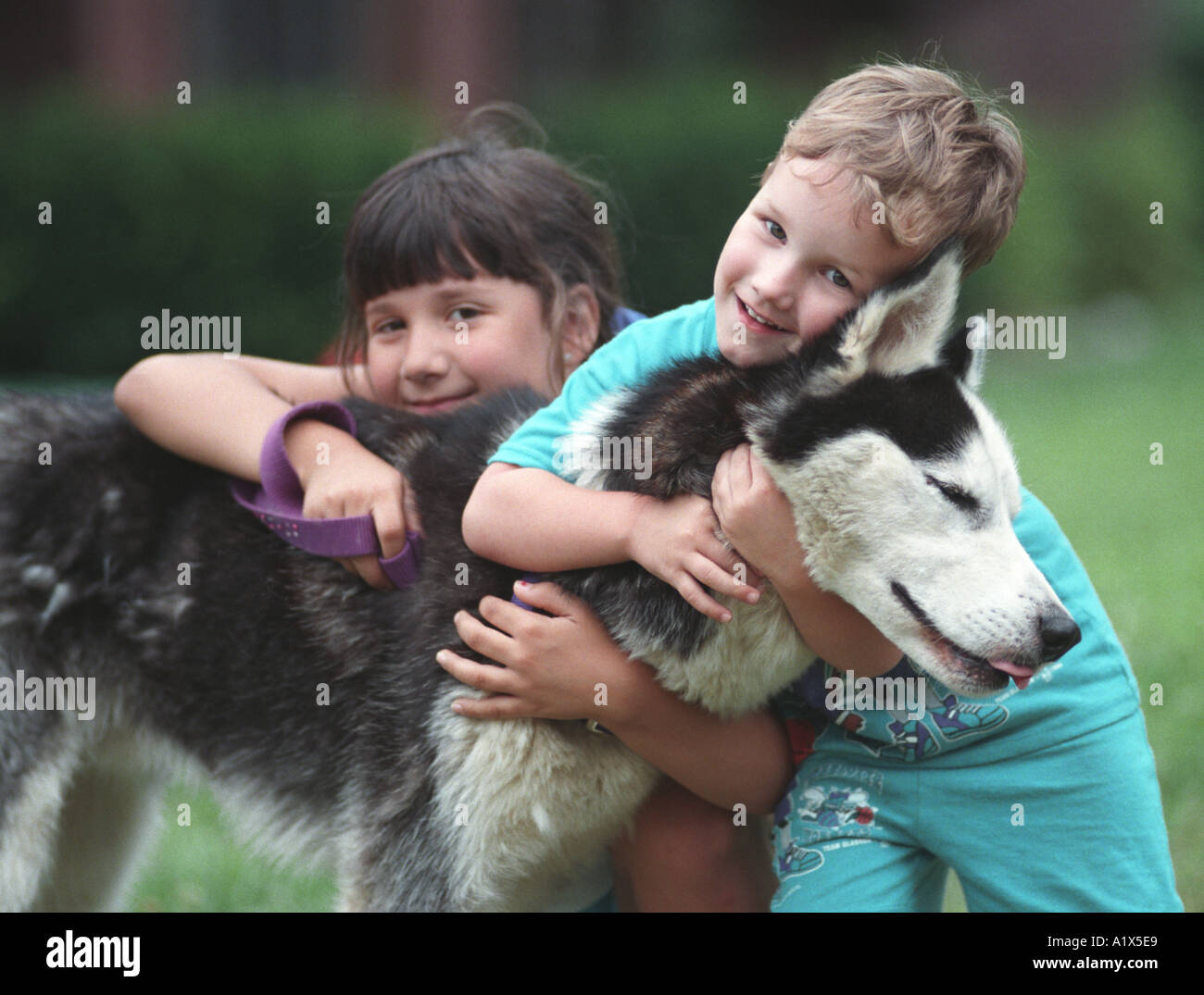 Two small children boy and girl hugging pet dog glee and joy on face  playing and family love Stock Photo - Alamy